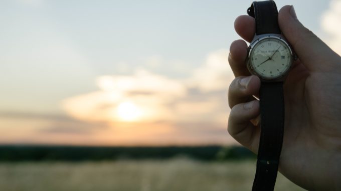 Person holding a watch with sunset in the background