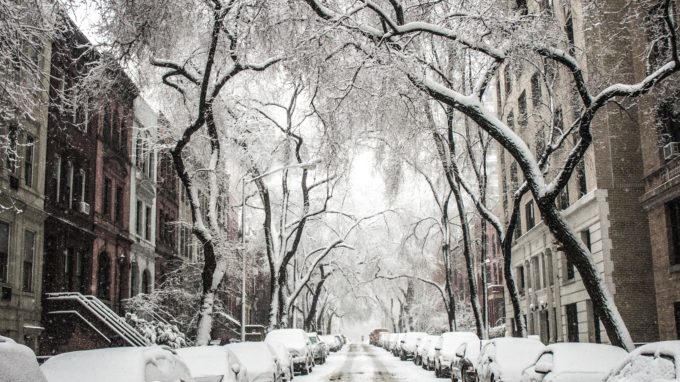 Street covered in snow with homes and cars on either side