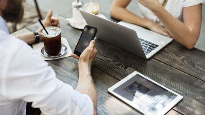 Two people at a table, one looking at a phone and the other at their laptop