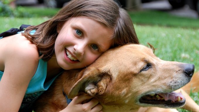 Young girl embracing pet dog.