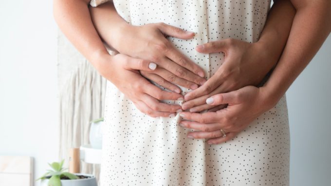 Pregnant couple embracing pregnant belly.