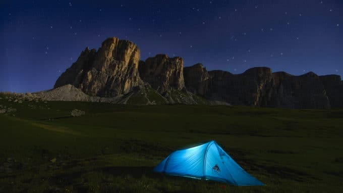 Blue tent in a field near the mountains on a starry night