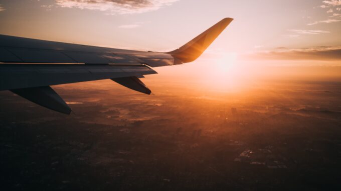 The wing of a plane with the sun setting behind