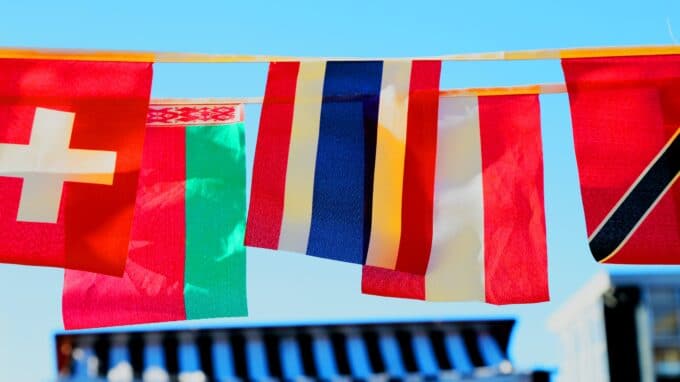 Different international flags hanging against a blue sky.