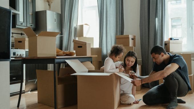 Two adults and one small child gathered around moving boxes in a kitchen.