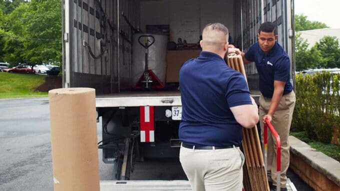 Two men unloading a large item from a moving truck.