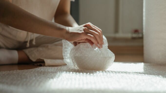 Person wrapping bowl with bubble wrap.