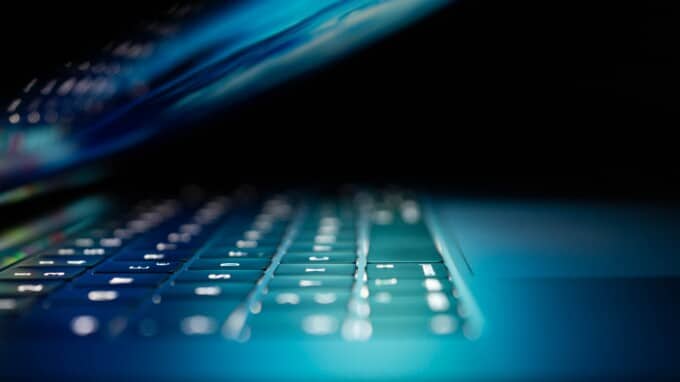 Laptop partially closed with keyboard illuminated against dark backdrop