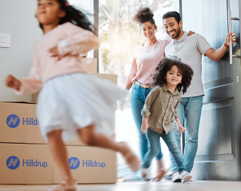 Family entering their new home with Hilldrup moving boxes in the background. 