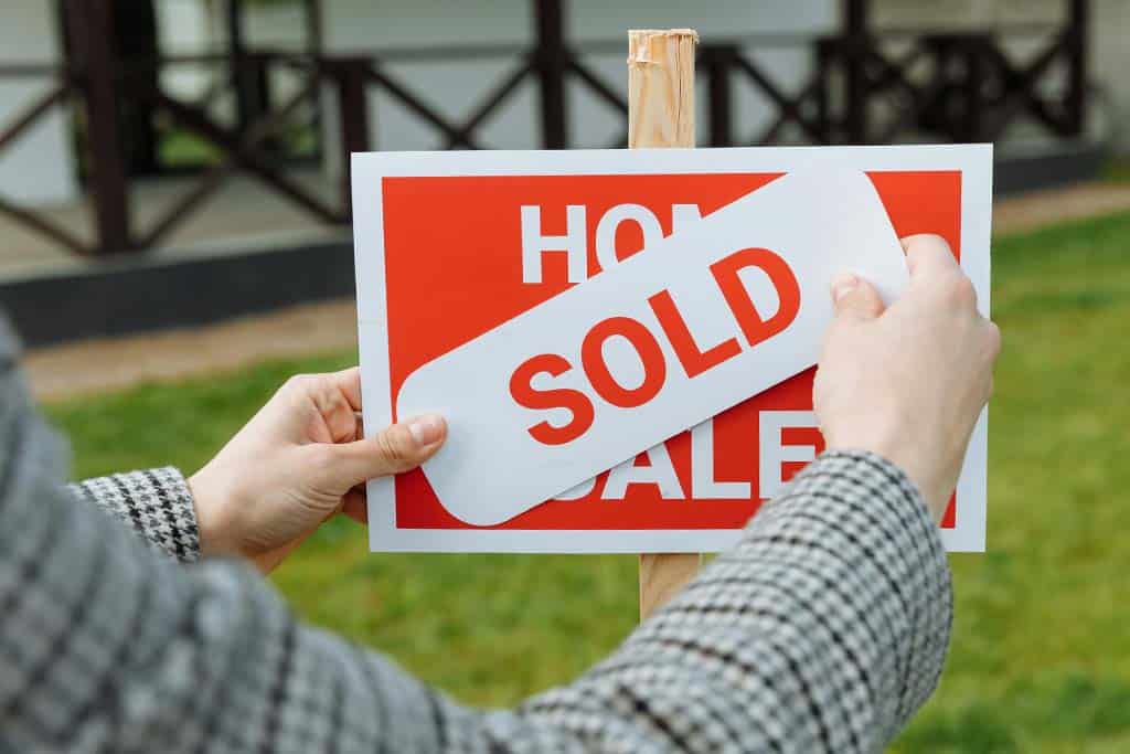 A home sale sign with a sold sign being attached to it. 