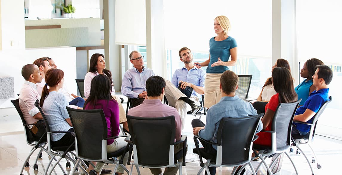 Female HR representative speaking to a team of employees who are seated around her in a circle