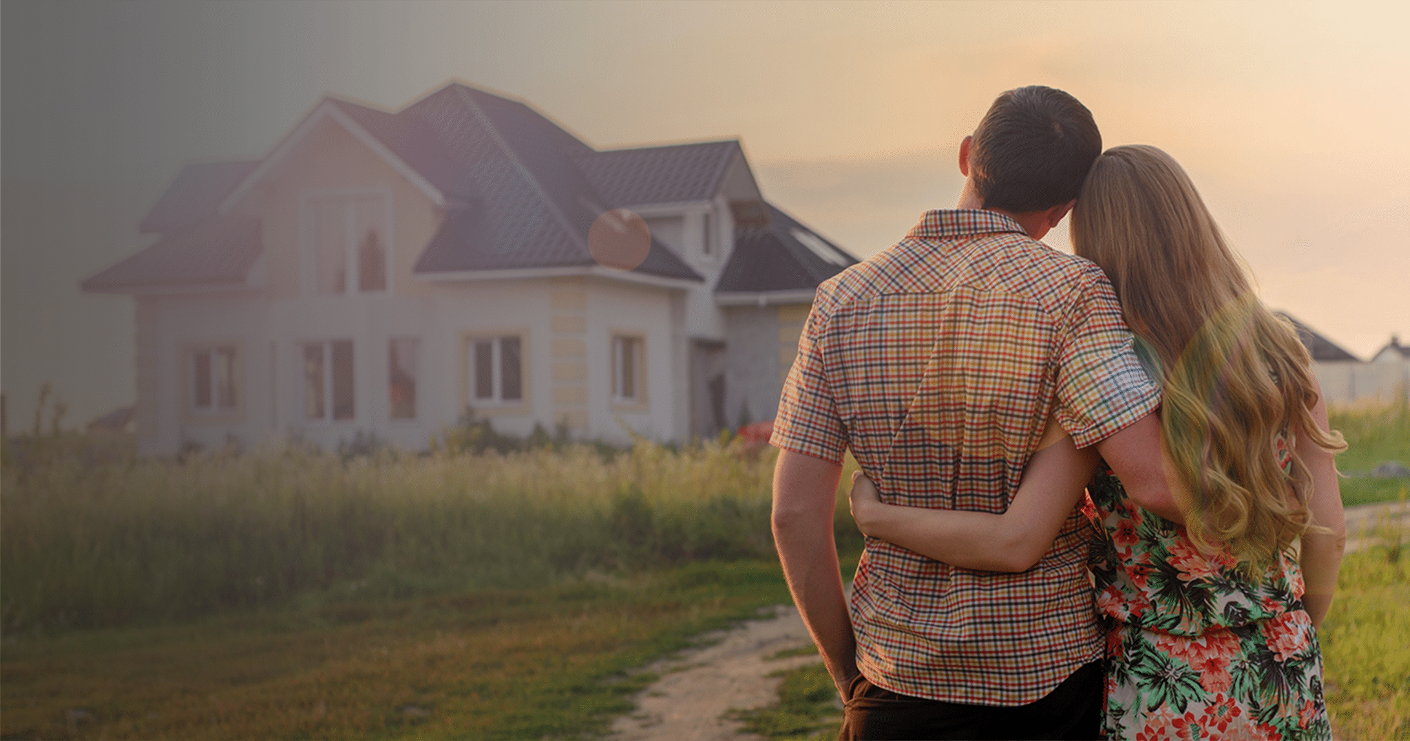 Couple standing with their back to the camera, outdoors, looking at a large house.